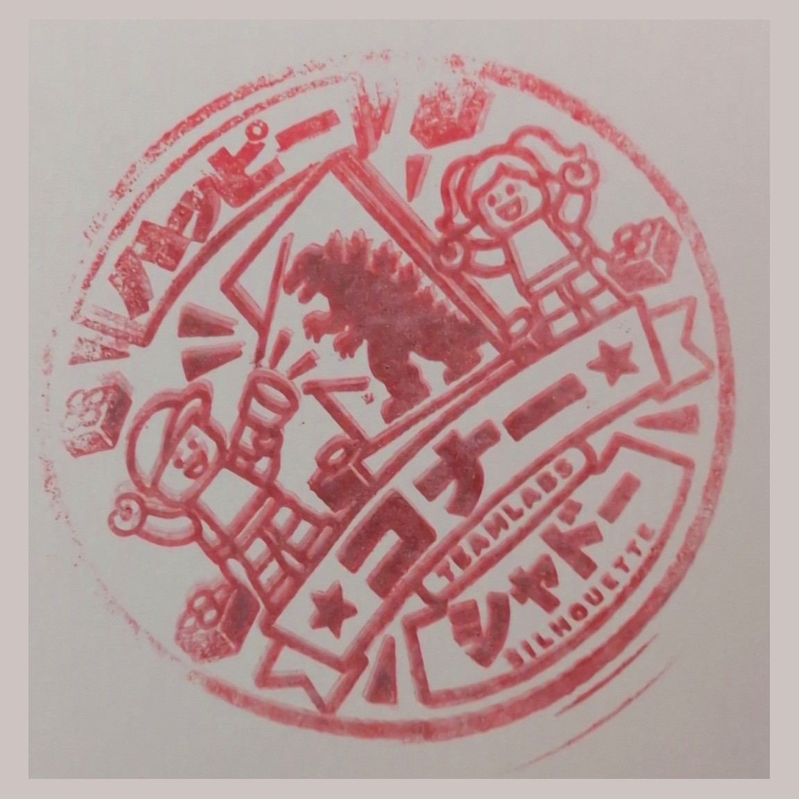 Ink impression of a stamp showing a Godzilla silhouette and two minifigures