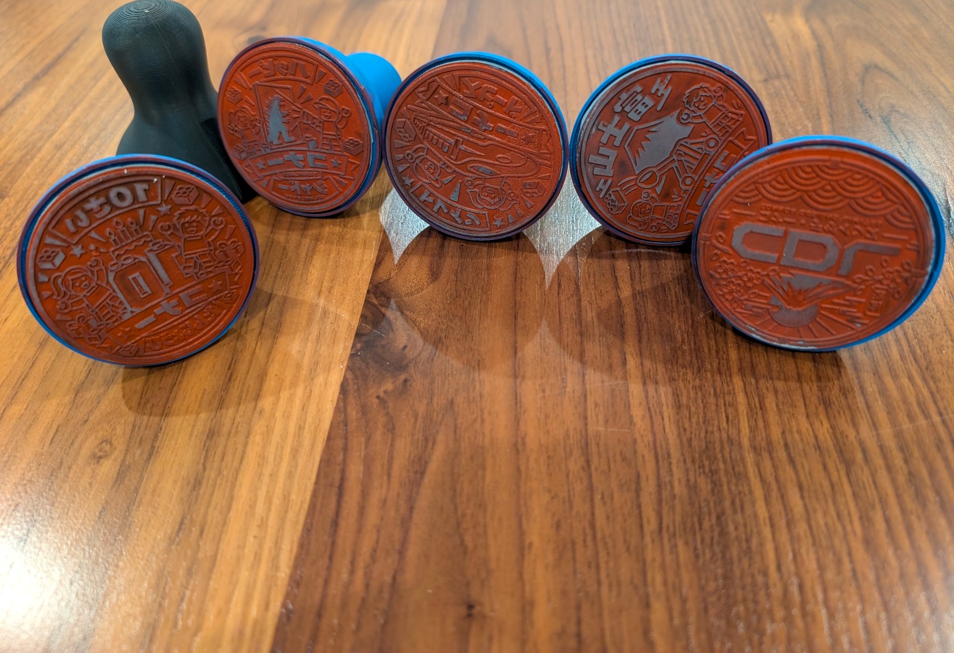 Six custom rubber stamps with engraved faces and 3D-printed handles arranged on a wooden table