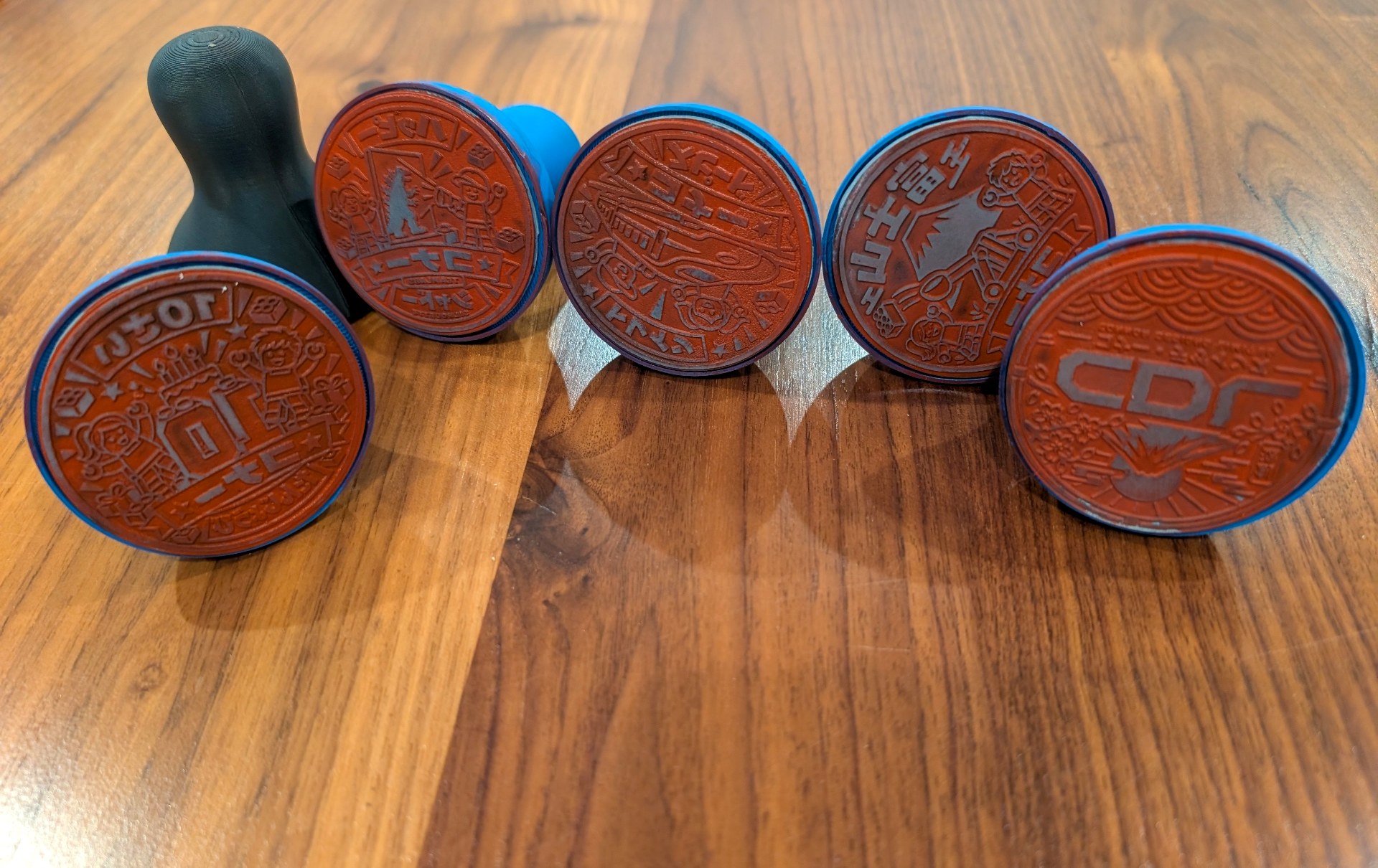 Five custom rubber stamps with engraved faces and 3D-printed handles on a wooden table